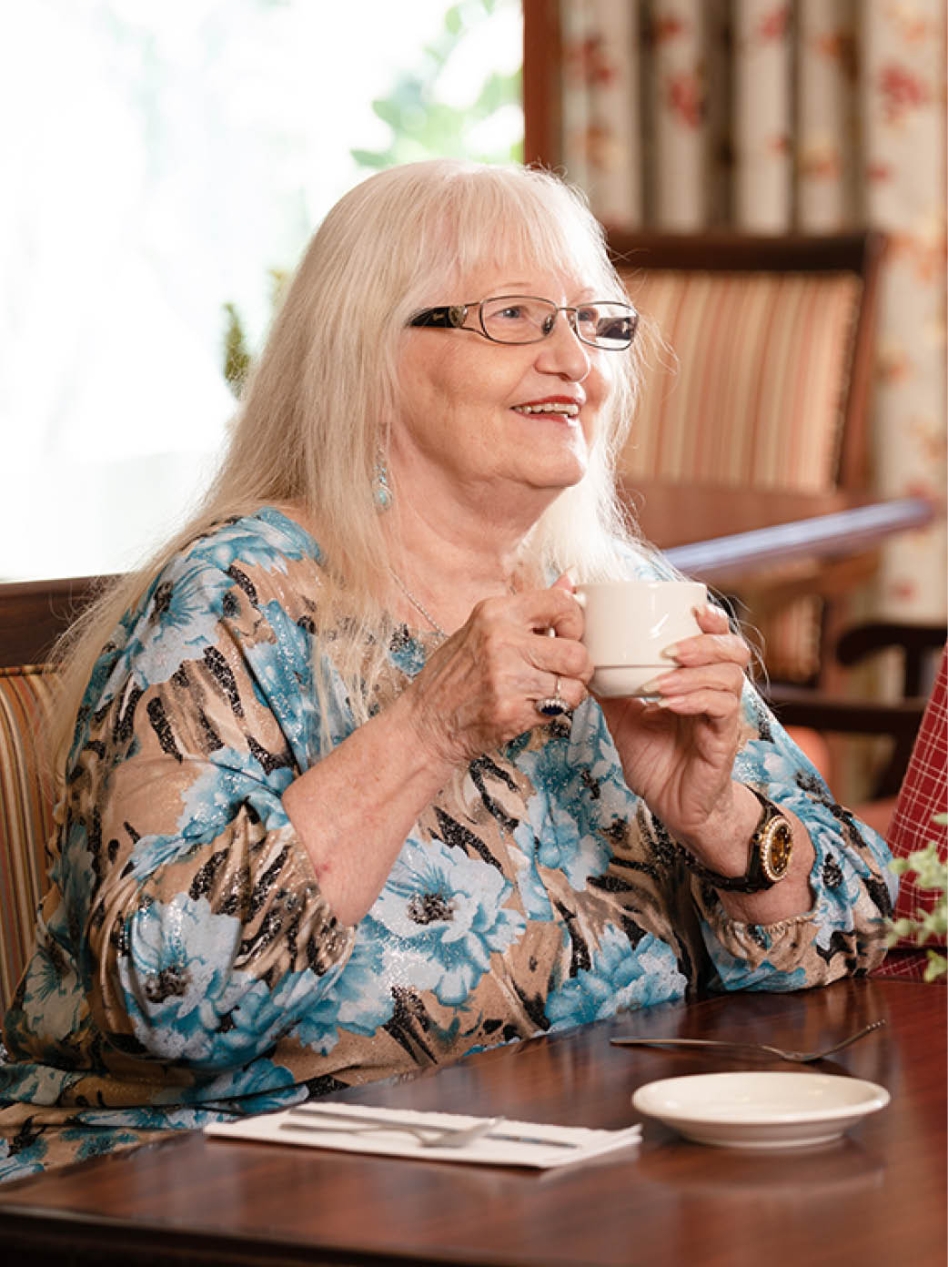 A female resident enjoys coffee in the dining room.